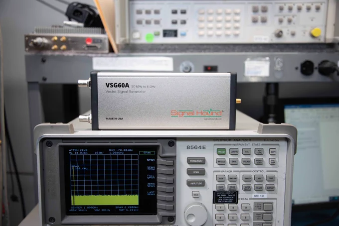 A close-up view of electronic test equipment, including a Signal Hound VSG60A Vector Signal Generator on top and a spectrum analyzer below in a laboratory setting.