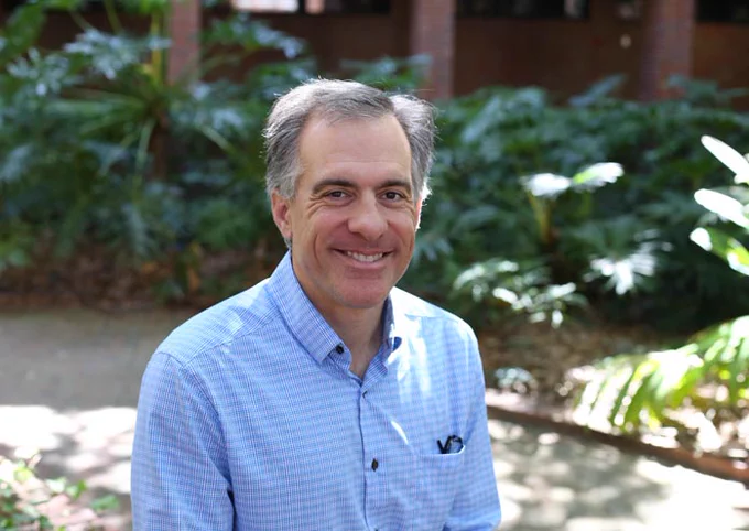 Sevan Terzian smiling at the camera against a background of greenery. He is wearing a blue shirt in what appears to be a staged situation. 