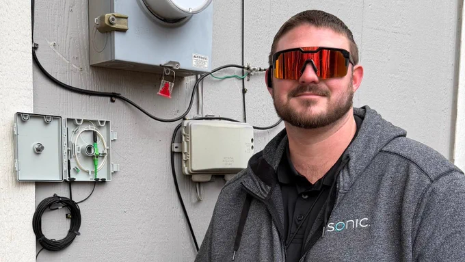 Sonic field service lead Austin standing and smiling in front of a transition box. Austin is wearing shades and repping the Sonic sweatshirt.