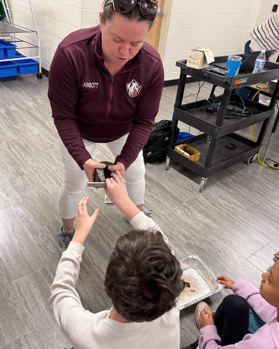 A woman in a maroon jacket helps pull apart strong magnets. 