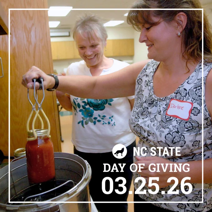 Woman using tongs to lift a jar of tomato sauce from a large pot in a kitchen setting.
