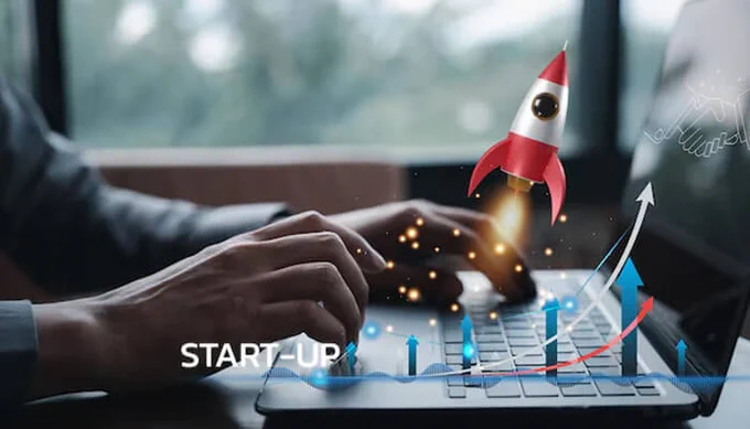 Startup growth concept showing a rocket launch above a laptop keyboard with upward trend arrows and business scaling visuals.
