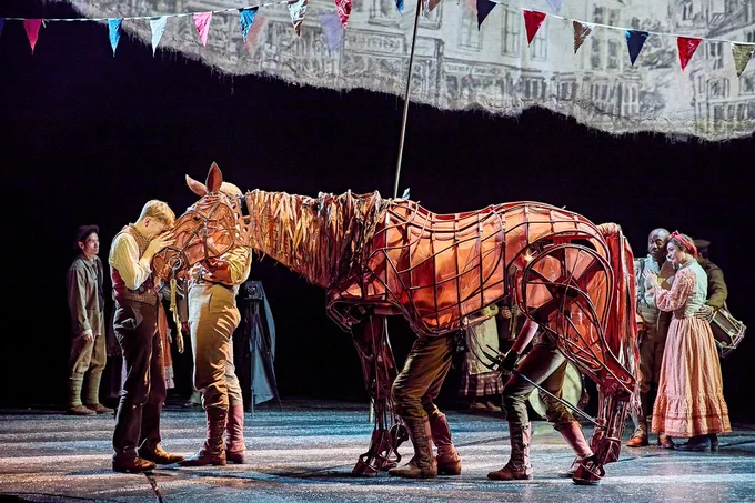 A boy kisses the head of Joey, a puppet horse