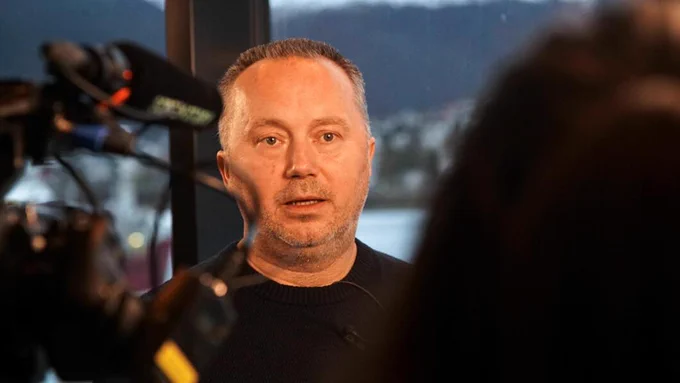 Human rights defender Tommy Olsen, a white man with short grey hair, is speaking to a journalist while recorded on camera.