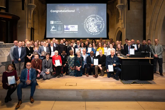 A large group of people standing and seated together on stage at the Greater Cambridge Design and Construction Awards ceremony. A presentation screen in the background reads ‘Congratulations!’ alongside event logos.