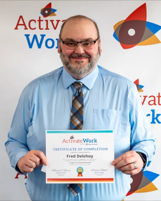 Fred Delehoy, wearing a blue shirt and tie, holding a certificate of completion from ActivateWork against a branded backdrop.