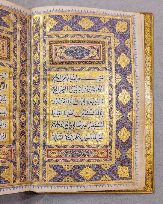 An ornately illuminated page from the Quran featuring intricate geometric and floral patterns in gold, blue, and red. Arabic calligraphy is elegantly inscribed within decorative borders, displaying traditional Islamic artistry.