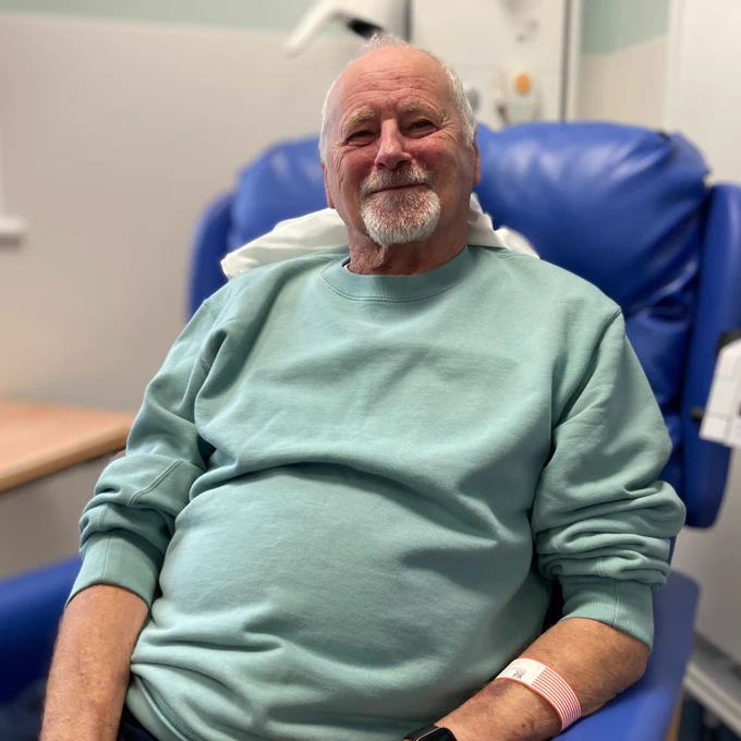 A photograph of Charles, wearing a green jumper, sat having immunotherapy.