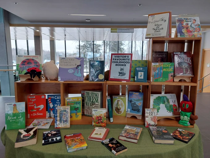 Display table with poster saying Visitor's Favourite Childhood Books and filled with kids books and puppets