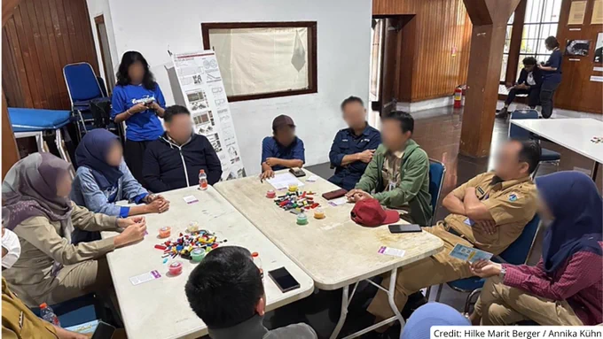 Group of people seated around a table engaged in a collaborative activity with colorful blocks and cards in a casual indoor setting.