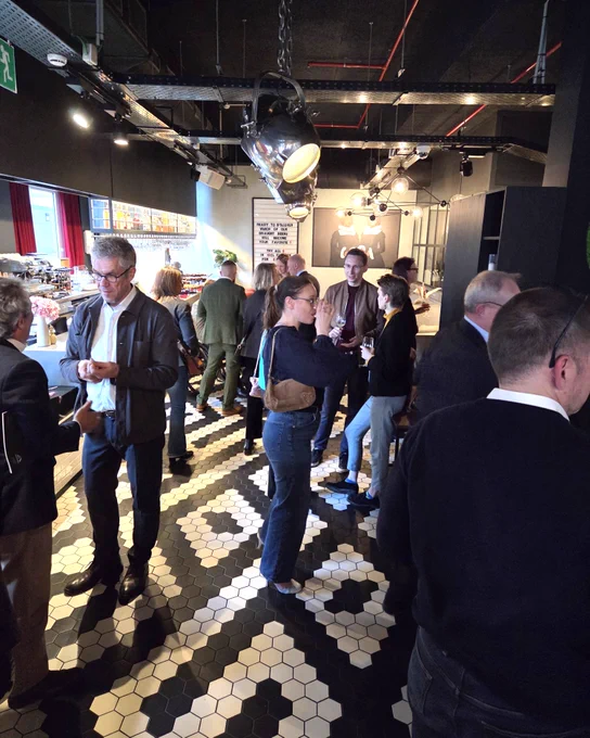 People socializing and networking in a modern cafe with black and white hexagonal tile flooring and industrial lighting.