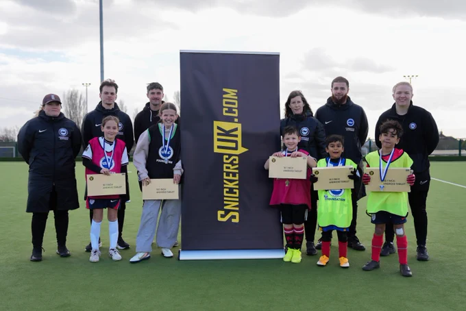 Foundation coaches and children that won player of the day stand either side of a SnickersUK banner