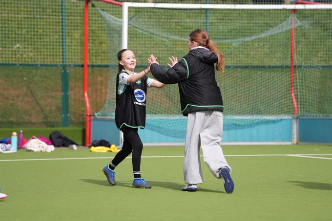 Two girls in black bibs smile and high five during a game