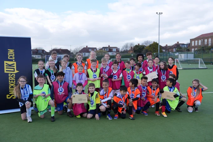 A large group of children wearing Brighton bibs and medals, stand next to a SnickersUK banner