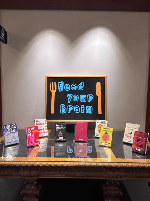 
A book display featuring nine titles: Polar War by Kenneth R. Rosen, How to Be a Rich Old Lady by Amanda Holden, The Science of Second Chances by Jennifer Doleac, Enshittification by Cory Doctorow, Football by Chuck Klosterman, All About Allergies by Dr. Zachary Rubin, and Everything is Tuberculosis by John Green. Signage reads, “feed your brain.”