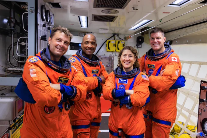 Four Artemis II NASA astronauts in orange space suits standing with arms crossed inside the white room on the crew access arm of the mobile launcher. Image Credit: NASA/Frank Michaux