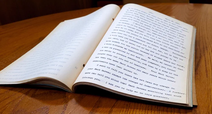Photo of a bound manuscript laid open on a table, the stenographic minutes of public hearings from March 20, 1934.