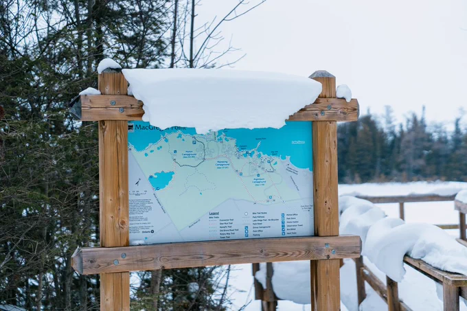 large wood sign with park map, snow on top of the wooden frame. 