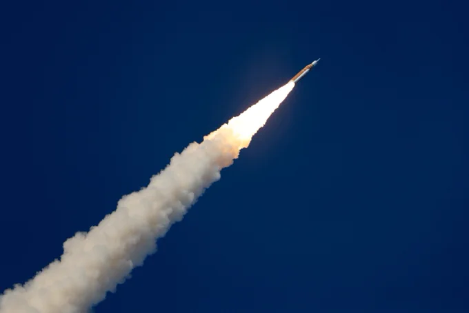 NASA\u2019s\u202FArtemis II SLS (Space Launch System)\u202Frocket, with the Orion\u202Fspacecraft atop carrying NASA astronauts Reid Wiseman, Victor Glover, and Christina Koch, along with Canadian Space Agency astronaut Jeremy Hansen, launches from NASA's Kennedy Space Center. Two white solid rocket boosters are on either side of the orange core stage. White plumes emit from the rocket engines. The sky is blue in the background. Credit: NASA/Michael DeMocker