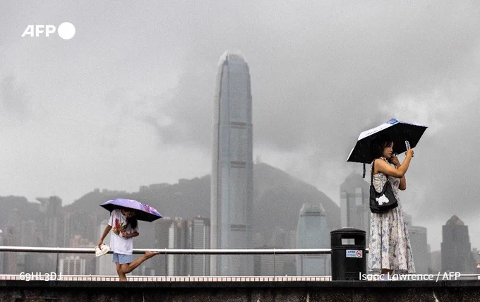 A woman takes a photo next to Victoria Harbour in Hong Kong on August 14, 2025, as Typhoon Podul weakens to a severe tropical storm.