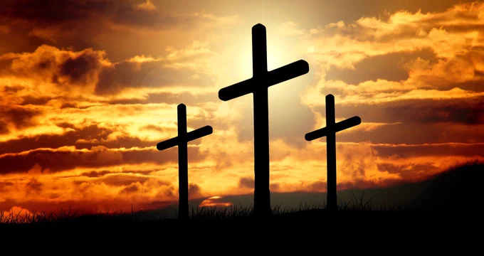 This image depicts a symbolic scene associated with Easter and Christian theology. It features three crosses silhouetted against a dramatic sunset or sunrise, with a vibrant sky filled with warm hues of orange, yellow and red. The central cross is larger, flanked by two smaller crosses, which represent the Crucifixion of Jesus Christ alongside the two thieves, as described in the New Testament (Luke 23:32-43). The setting sun or rising sun can symbolize themes of death and resurrection, central to the Easter narrative, which commemorates Jesus' crucifixion on Good Friday and resurrection on Easter Sunday. The overall mood of the image is sombre yet hopeful, reflecting the duality of sorrow and triumph in the Easter story.