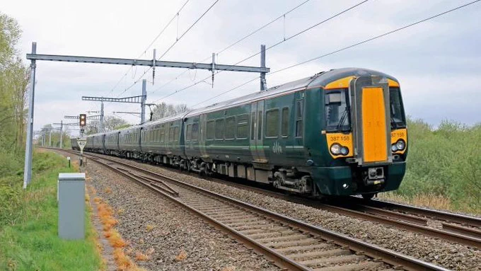 a green suburban train with a blunt yellow nose running through countryside 
