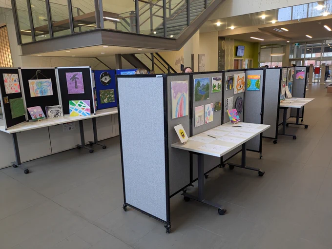 An art gallery setup in the main lobby of Ron Joyce Children's Health Centre, with tables and folding display panels set up with colourful artwork of all kinds.