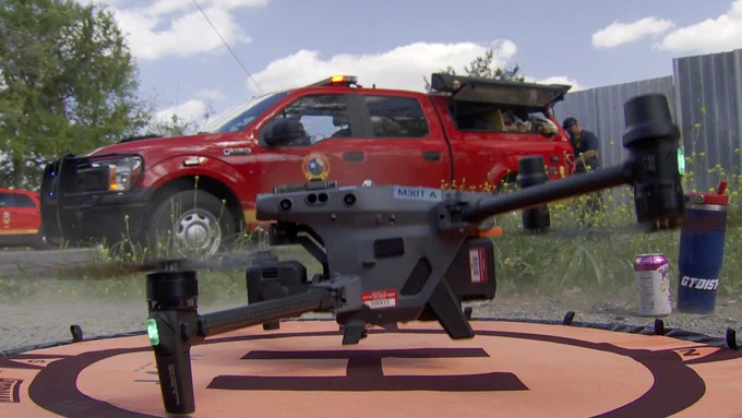 A drone sits on a landing pad in front of a command vehicle.