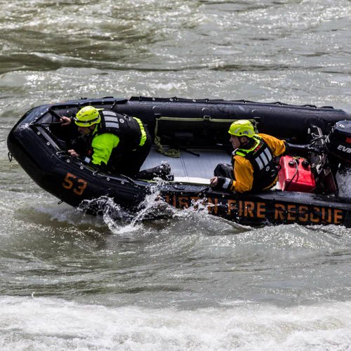 Two firefighters operate a boat on rough waters.