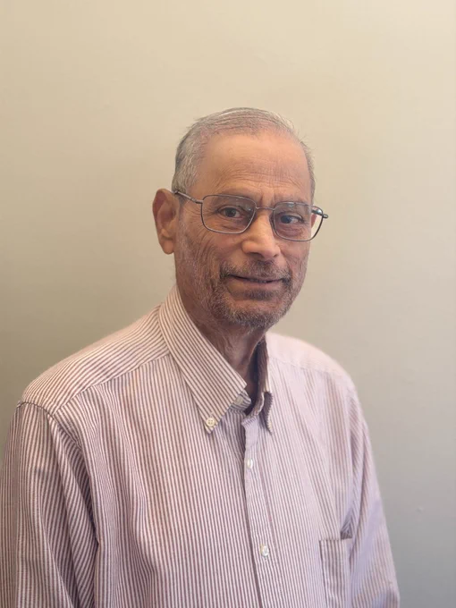 Distinguished Professor Sreenivasa Rao Jammalamadaka looking forward with a gentle smile, wearing a maroon and white striped shirt.
