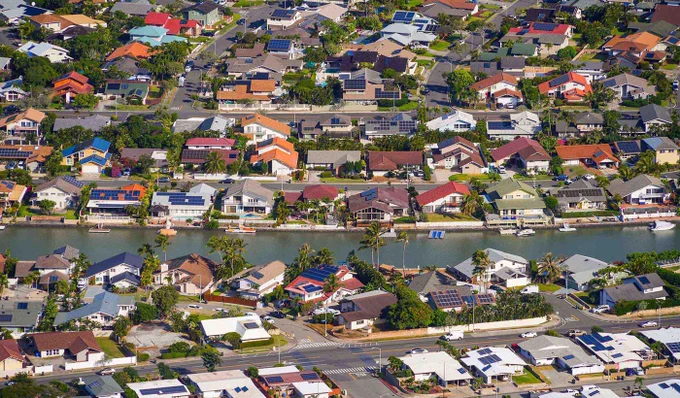 Aerial view of a suburban neighborhood with houses lining a canal, featuring docks and boats along the waterway.