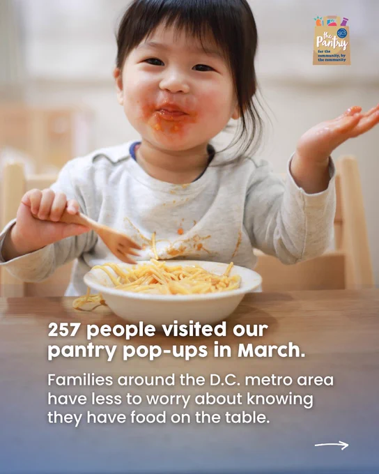 A young child sits in a high chair, smiling with sauce on their face while eating a bowl of spaghetti.