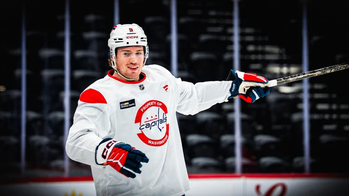 Ryan Leonard smiles and points his hockey stick towards the ice.