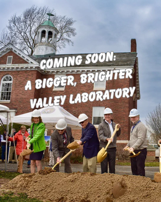 Five people ceremoniously digging into a pile of dirt in front of the Valley Laboratory. Words across the image say Coming Soon: A bigger, brighter Valley Laboratory.