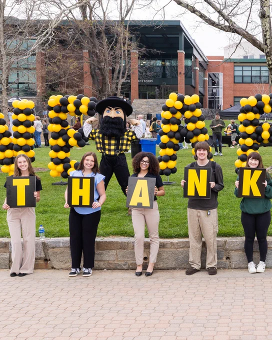 Group of students standing in front of black and gold balloon letters spelling “THANK,” with the Yosef mascot posing behind them on Sanford Mall during Appalachian State Giving Day.