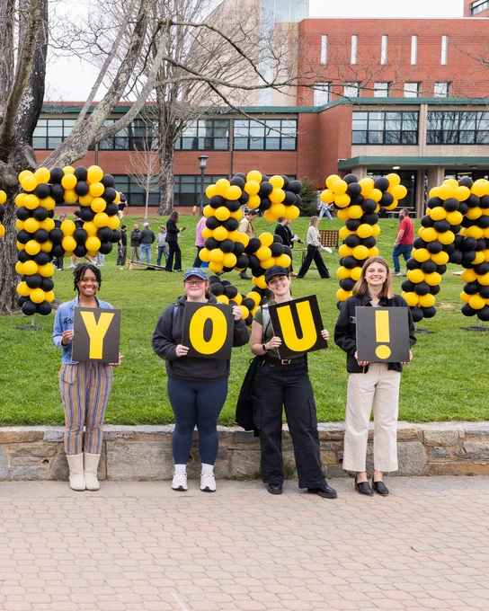 Group of students holding letter signs that spell “YOU!” in front of black and gold balloon letters on Sanford Mall, thanking supporters during Appalachian State Giving Day.