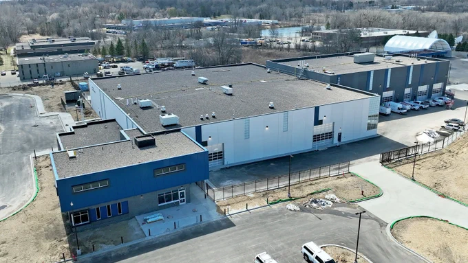 new building under construction with three sections from left to right of blue, white and gray with landscape in back