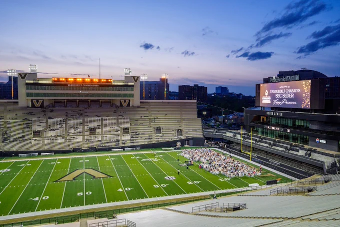 An aerial shot shows students gather on the field of FirstBank Stadium. 