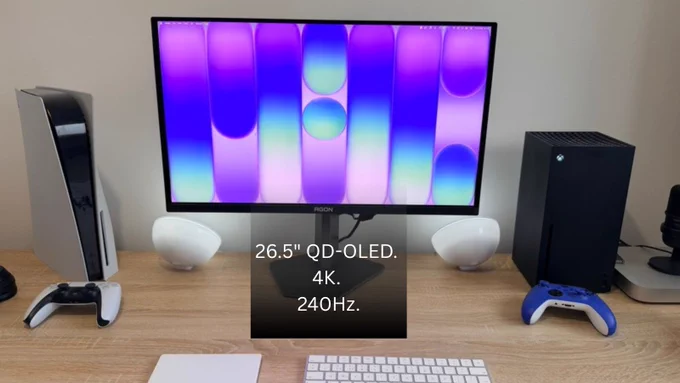 Desk setup with 26.5‑inch QD‑OLED 4K 240Hz monitor showing colorful wallpaper, flanked by a PS5 and Xbox Series X with controllers.
