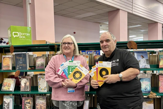 Ian right in a black RNIB shirt & Paula chapman from high life highland libraries pose with various information brochures