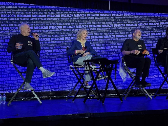 Brent Spiner in jeans and black hoodie from his podcast, Gates McFadden in jeans, Bev shoes (by shoesbyjax), blue jacket and light grey hoodie, Jonathan Frakes in black jeans and shirt from his podcast with Spiner. 
The three are sitting on director's chairs on stage, while laughing at something Spiner said.