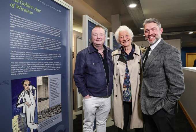 Three people stand indoors in front of an exhibition panel titled “The Golden Age of Wireless.”