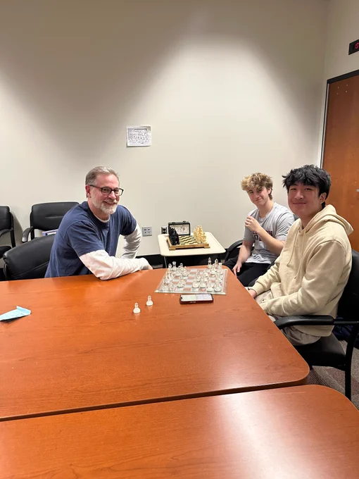 a student and teacher playing chess while another student is watching