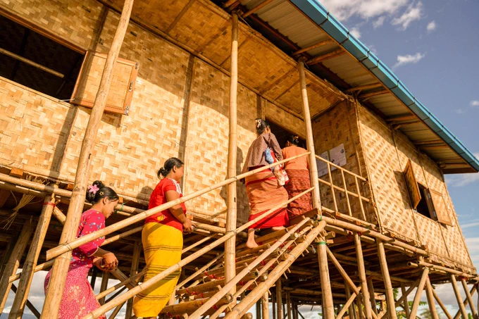 Family members and neighbours visit the new stilt house, carrying household items and offerings in Myanmar.
