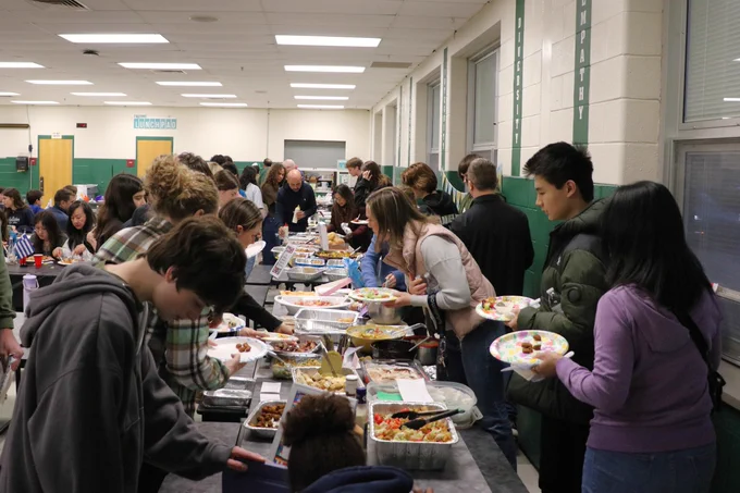 People serving themselves food from a buffet line in a stetson cafeteria with green and white walls.