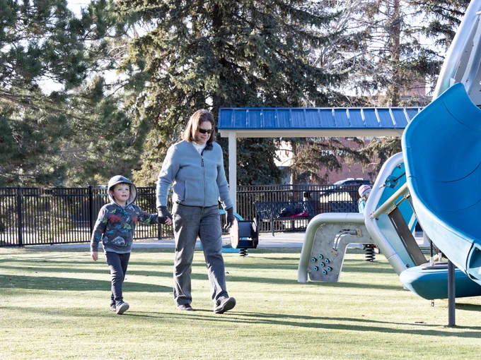 A woman and young boy walk along the turf at an outdoor park. 
