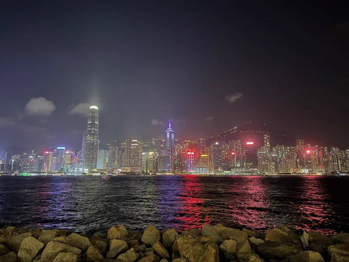 Hong Kong Island skyline in the night. Neon lights beam into the sky and glitter across the water.