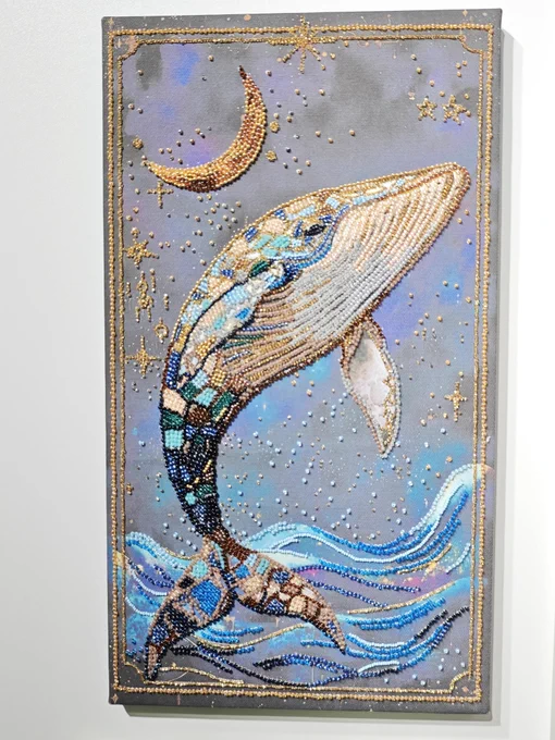 A vertical mixed-media canvas painting of a humpback whale breaching over ocean waves under a golden crescent moon. The whale, waves, and moon are intricately handcrafted using rows of colorful beads, creating a 3D textured effect against a painted blue and purple background with gold beaded stars.