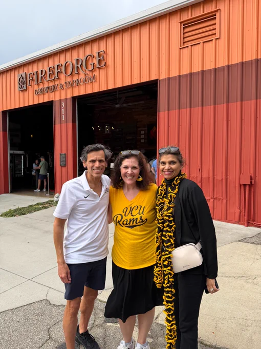 A woman in a gold V-C-U Rams shirt with Dr. Rao and Monica Rao on either side of her, all smiling. Behind them is Fireforge Brewery & Taproom.