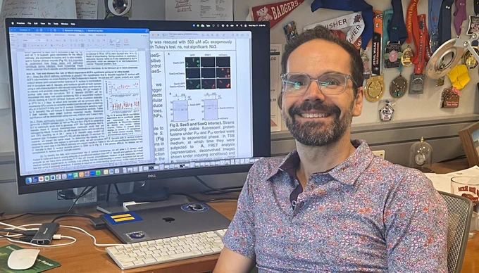 Georgetown biology professor Shaun Brinsmade smiles in front of a computer.